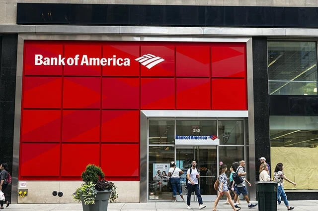 people walk outside of a bank of america branch on a sunny day.