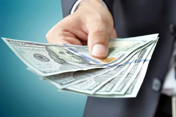 a man in a business suit holds out several hundred dollar bills.
