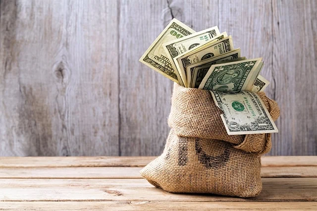 Buy 'The Future': 5 Tech Stock ETFs You Should Own 7 money in a sack sitting on a wooden table.