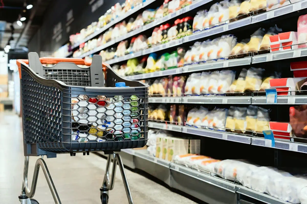 June CPI: Inflation Speeds Up, Tariffs Starting to Creep In 2 a gray grocery cart sits near a cold-foods aisle.