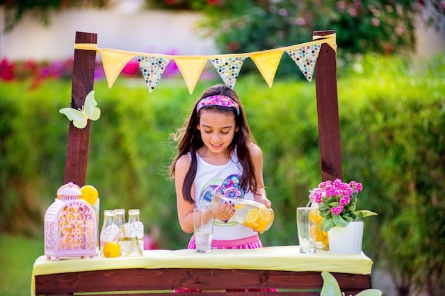girl pouring lemonade at a lemonade stand.