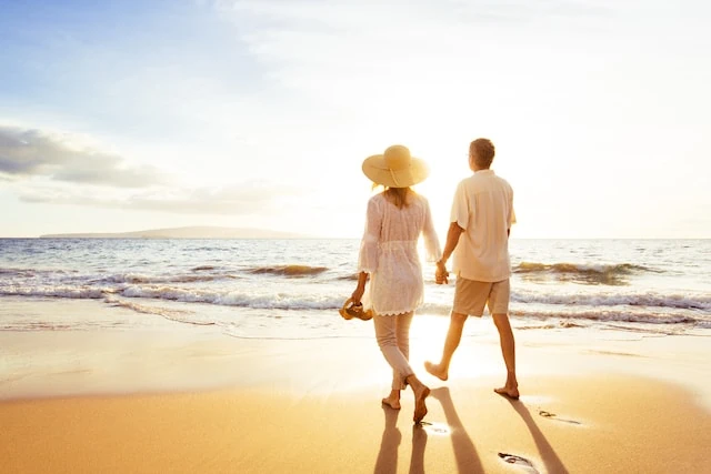 Should You Ease Into Retirement? These Are the Pros + Cons 2 Mature Couple Walking on the Beach at Sunset