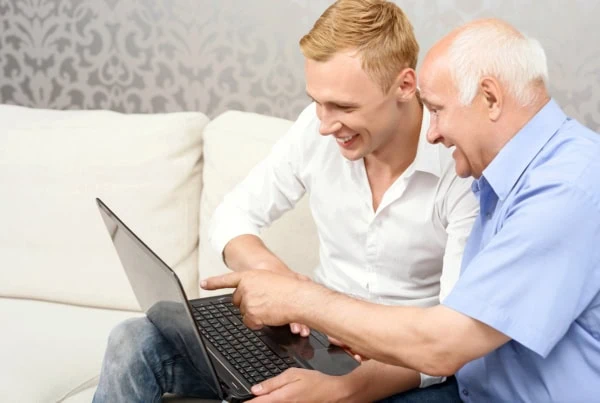 a young man and an older man smile while looking at a laptop.
