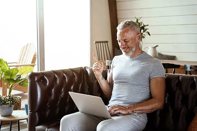 an older, fit man wearing a gray shirt looks at his laptop.